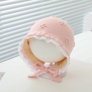 Detail of pink knitted baby bonnet with white lace trim and secure chin straps