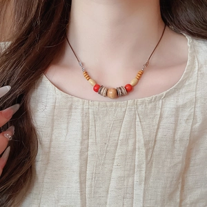 Détail d'un collier ethnique fait main avec perles en bois et accents rouges sur mannequin