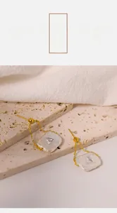 Macro detail of gold geometric earrings with square shell charms on a stone surface
