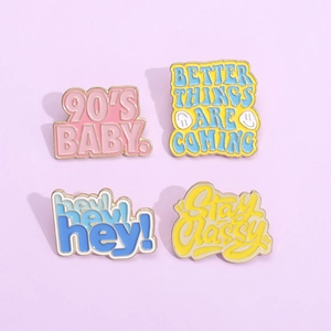 Close-up of four colorful enamel lapel pins with motivational English quotes on lilac background