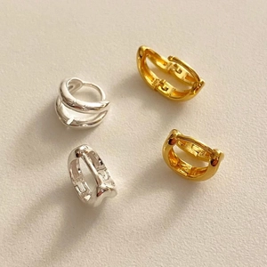 Close-up of S925 sterling silver and gold layered hoop earrings on textured beige background