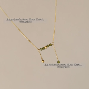 Macro detail of 18K gold-plated necklace with olive green crystal beads and twin tassels