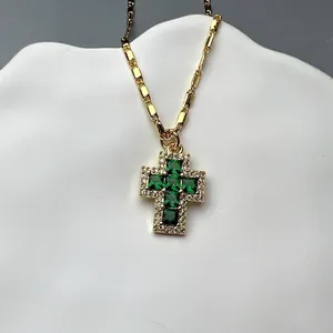 Detail shot of a gold-plated cross necklace with a central green zircon gemstone