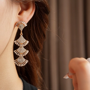Close-up of four-layer fan-shaped tassel earrings with inlaid crystals on a gold base