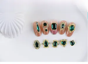 Detailed view of emerald green nail gems in various shapes with gold alloy borders
