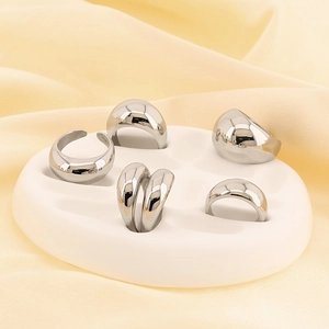 Macro detail of five silver polished stainless steel rings on pebble display with silk cloth