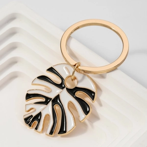 Golden monstera leaf keychain with black and white enamel finish on a white display base