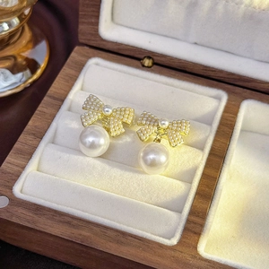 Detail of elegant gold bow earrings with micro pearls and large white pearl drops
