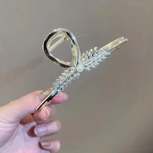 Detailed macro view of a gold-finish hair claw clip with rhinestones and a white pearl