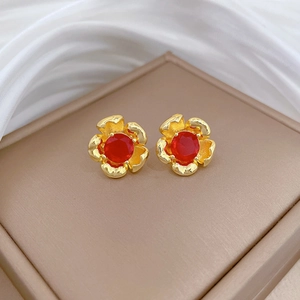 Macro detail of red rose floral earrings with gold plating on premium silk background