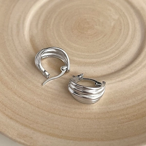 Detail of silver twisted hoop earrings with multi-layered texture on wooden tray
