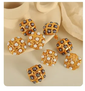 Detailed view of square woven gold earrings with inlaid white and grey pearls