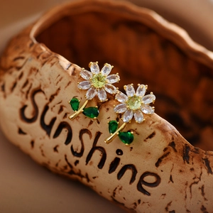 Macro shot of gold-plated daisy earrings with green and clear marquise gems