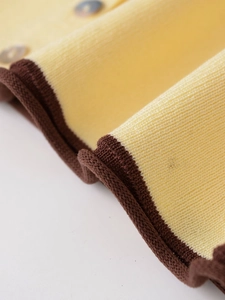 Détail du tissu en maille jaune avec bordure marron contrastée et boutons en nacre