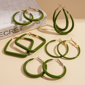 Orecchini a cerchio in resina verde geometrica con dettagli in metallo su libro beige