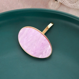 Close-up of pink marble acetate oval hair clip with gold metal frame on ceramic plate