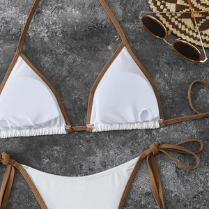 Flat lay of white bikini set with brown straps, sun hat, and sunglasses on stone background