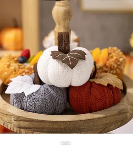 Detailed close-up of knitted pumpkin decorations in grey and red on a rustic wooden tray