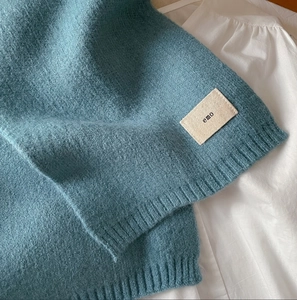 Close-up of soft blue knit scarf fabric featuring an 'emo' woven label detail