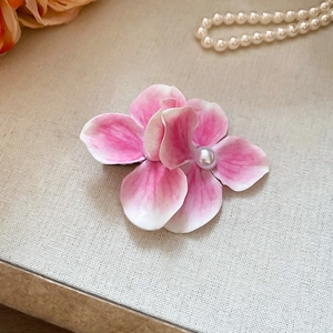 Detailed close-up of a pink floral hair clip with a pearl center on a soft fabric texture