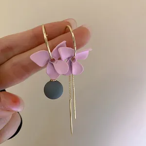 Detail of asymmetrical pink flower earrings with golden tassels and matte petal texture
