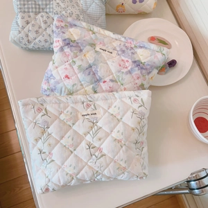 Quilted floral and checkered cotton cosmetic bags in pink and blue displayed on a desk