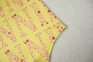 Close-up of yellow fabric with pink dotted N-letter prints and reinforced stitching detail