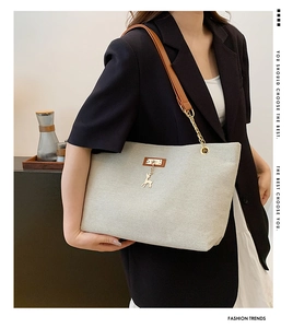 Detail of beige canvas tote bag with brown leather straps and gold deer charm pendant