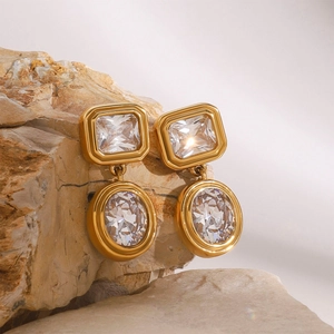 Detail of gold earrings with rectangular and oval white zircons on natural stone