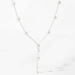 Détail du collier en Y en acier inoxydable avec perles blanches sur fond blanc minimaliste