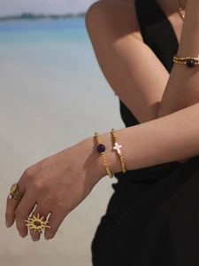 Detail of gold beaded bracelets with a cross pendant and sun-shaped ring on a model