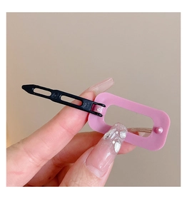 Close-up of a pink heart-shaped hair clip with a black base held by hand on neutral background