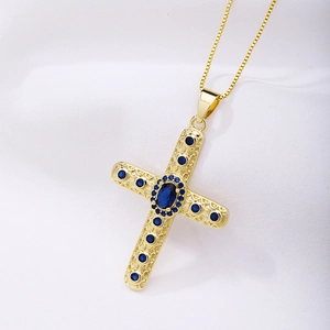 Close-up of golden cross necklace with blue oval gemstone and intricate filigree details