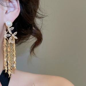 Close-up of gold flower tassel earrings with pearls on a model in warm lighting