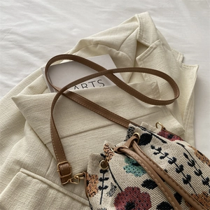 Ethnic knit bucket bag with floral pattern and brown strap on a beige blazer