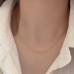 Detail of a gold-plated paperclip chain link necklace worn over a white shirt