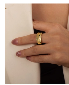 Dettaglio di un anello dorato vintage con pietre verdi, indossato da una modella in blazer