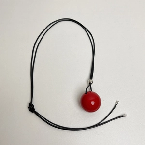 Minimalist red geometric ball pendant necklace with adjustable black cord on white backdrop