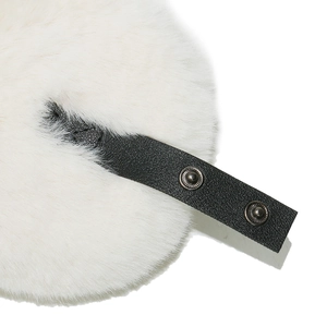 Macro detail of white faux fur winter hat featuring black leather strap and metal snaps