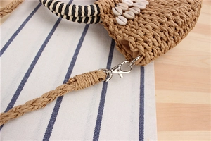 Close-up of semi-circular woven straw bag with shell decor and striped handle details