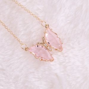 Close-up of a pink butterfly pendant with gold chain on white plush background