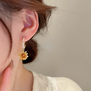 Close-up of gold sunflower earring with pearl detailing worn by a female model