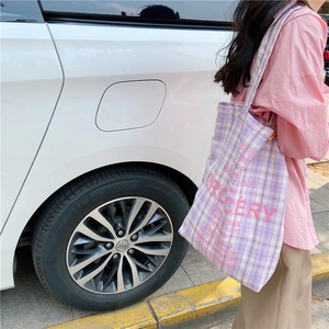 Close-up of lilac checkered canvas tote bag featuring pink Grocery text on street background