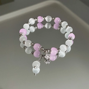 Makroaufnahme von Opal-Perlenarmband mit Blumenanhänger auf einer reflektierenden Spiegelfläche