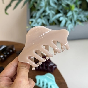 Détail d'une grande pince à cheveux rose chair tenue à la main sur un bureau en bois