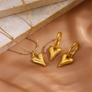 Polished gold heart pendant necklace and earrings set on champagne satin and stone