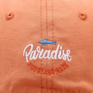 Dettaglio del cappello arancione in tela con ricamo a squalo e scritta logo Paradise