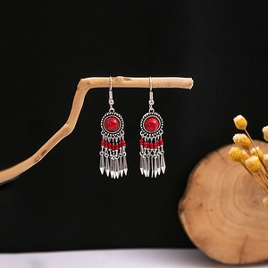 Close-up of bohemian earrings with red beads and silver tassels on wood branches