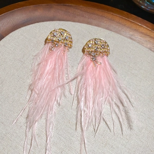 Detail view of pink feather tassel earrings with sparkling rhinestones on grey linen