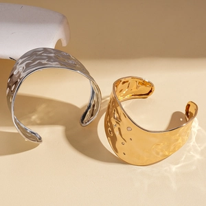 Irregular wavy gold and silver open bangles with hammered texture on a stone pedestal